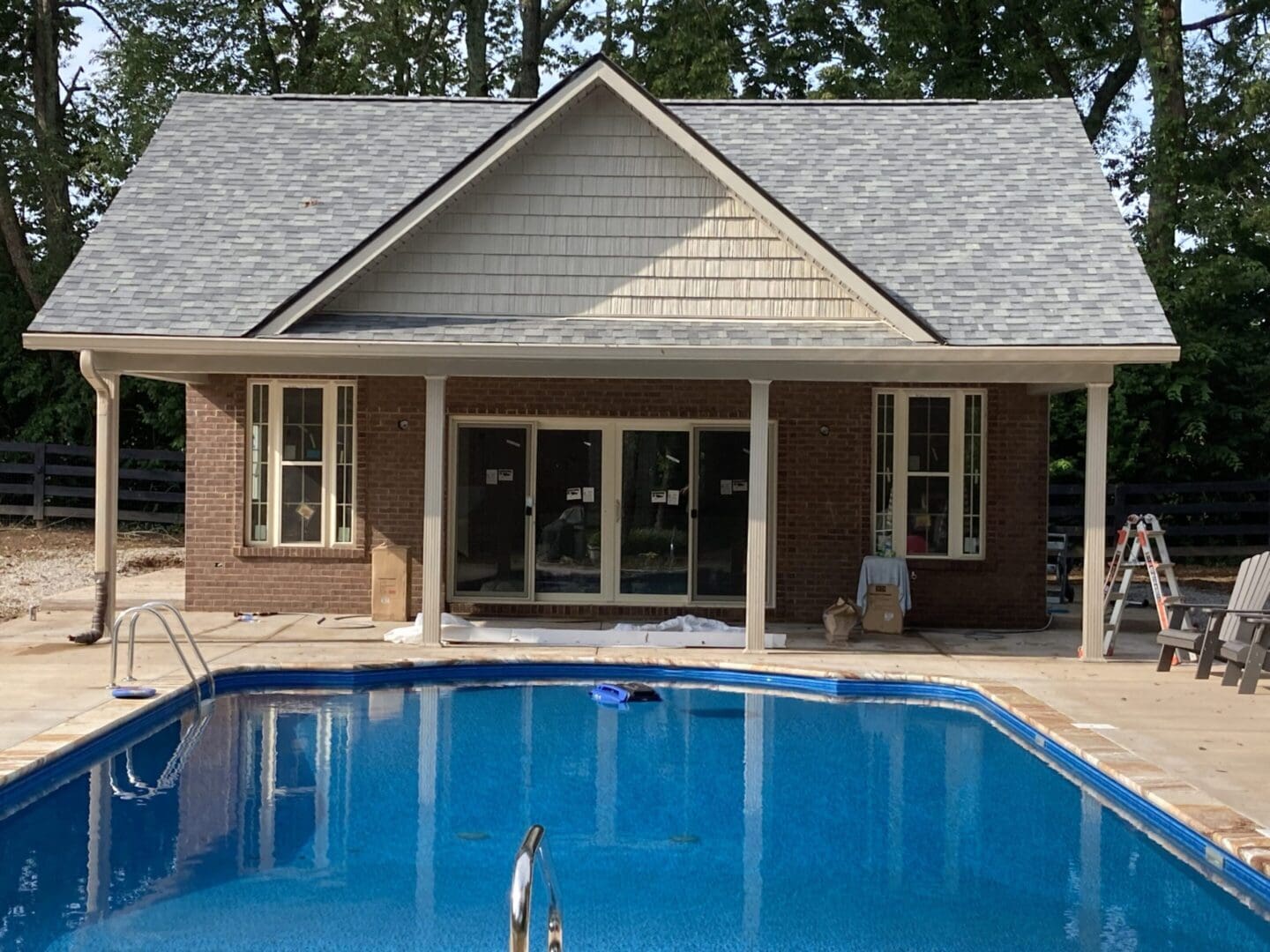 A backyard swimming pool with a brick house and sliding glass doors.